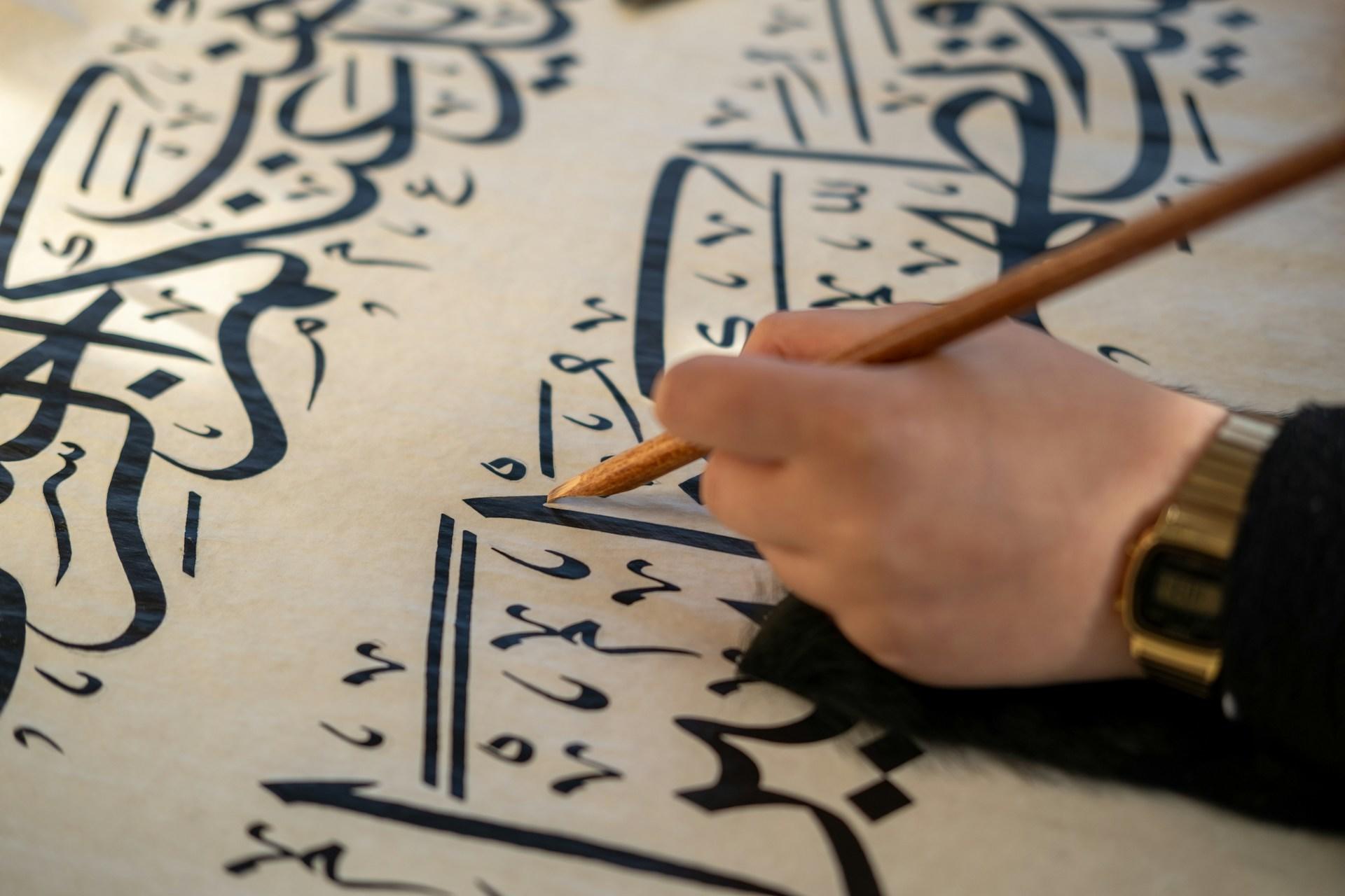 Main tenant un qalam en train d'écrire une calligraphie arabe sur papier nacré